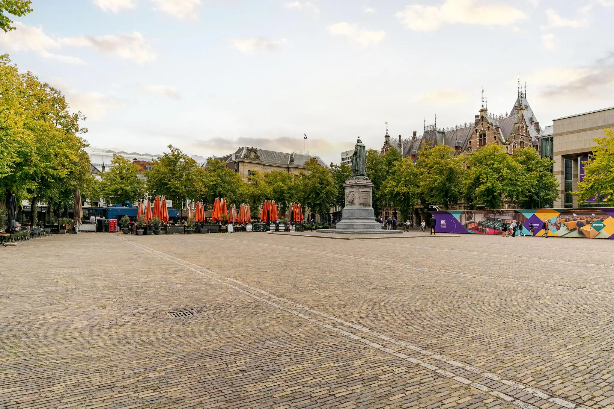 Plein met standbeeld en terrassen met oranje parasols aan het Lange Voorhout in Den Haag.